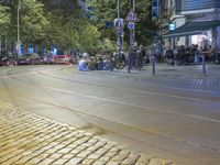 a street corner with cars and some lights and people on the sidewalk waiting to cross the road