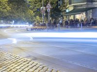 a street corner with cars and some lights and people on the sidewalk waiting to cross the road