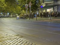 a street corner with cars and some lights and people on the sidewalk waiting to cross the road