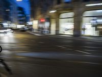 a man riding his bike through the streets at night, with cars coming by and buildings in the background