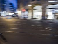 a man riding his bike through the streets at night, with cars coming by and buildings in the background