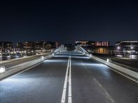 a very long bridge at night over the road and to many buildings in the background