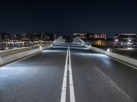 a very long bridge at night over the road and to many buildings in the background