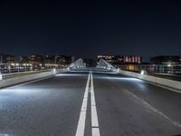 a very long bridge at night over the road and to many buildings in the background