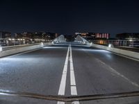 a very long bridge at night over the road and to many buildings in the background