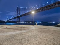 a couple of benches sitting under a bridge at night by water and lights in the air