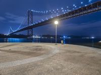 a couple of benches sitting under a bridge at night by water and lights in the air