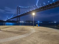 a couple of benches sitting under a bridge at night by water and lights in the air