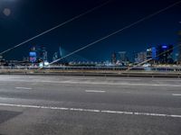 a road with buildings in the distance near by in a city at night time with full moon