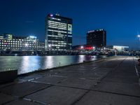 an empty walkway on the riverfront at night with a view of large buildings in the background