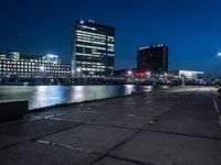 an empty walkway on the riverfront at night with a view of large buildings in the background