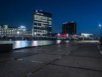 an empty walkway on the riverfront at night with a view of large buildings in the background