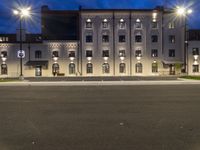 an empty street next to a large building at night with multiple lights on the windows