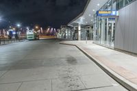 a bus stop next to a subway train depot on the street at night with lights on