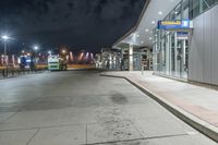 a bus stop next to a subway train depot on the street at night with lights on