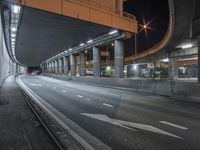 empty street next to tunnel and freeway under a bridge at night time as cars drive underneath it