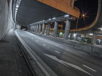 empty street next to tunnel and freeway under a bridge at night time as cars drive underneath it