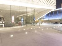 the front entrance of a modern glass building with columns and lights around it and a car parked in front