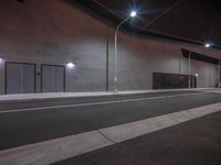 a empty street with a light pole at the side and building at the back lit up at night