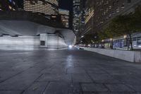 a city with a building in the background with some steps lit up at night as people sit on benches and tables near it