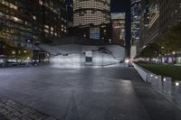 a city with a building in the background with some steps lit up at night as people sit on benches and tables near it