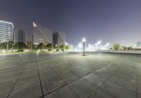 empty city plaza at night with the city lights on all around it, and skyscrapers in the background