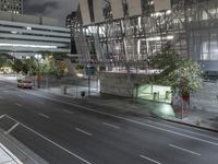 an empty road by a building with tall windows at night time on the other side
