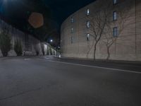 a dark road at night, with light shining on the wall and the street lamp