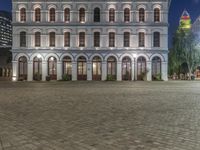 an older building with arched doors, in a city at night, and lit up