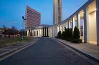 a building near an empty park at dusk with lights on and two buildings in the distance