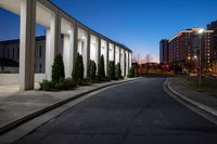 a building near an empty park at dusk with lights on and two buildings in the distance