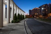 a building near an empty park at dusk with lights on and two buildings in the distance