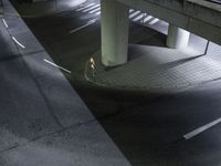 a man walking on the side of a road at night under an overpass above a sidewalk