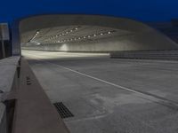 a concrete tunnel at night in the city, illuminated up by street lights and recessed on overhead