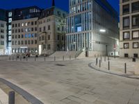 an empty city square with multiple buildings in it at night, a traffic light illuminates the center of it