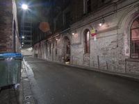 an empty city street at night with some buildings and a green garbage can near the curb