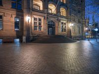 a night time image of an old style building, with stairs leading up to a stone stairway and large arched doorways, in a quiet city park setting