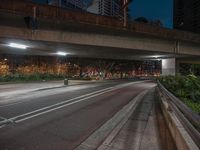 an empty city street at night with no traffic in it's lane and a bridge