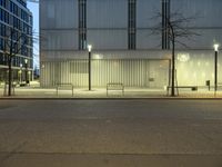 a paved street in the middle of buildings with tall windows at night, with car lights on