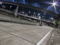 a man is riding his bike on a concrete road at night by some bridge lights