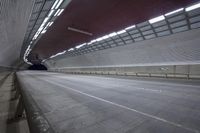 a man with a suitcase is walking across an empty road in a tunnel with metal structure