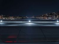 an empty parking lot near some street lights and buildings with lights reflecting on it and a river running under the roof