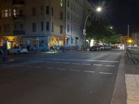 a road at night in front of an apartment building on a street corner, with police tape running beside the road