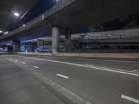 an empty street and two highway overpass at night time and light signs in the background