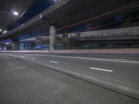 an empty street and two highway overpass at night time and light signs in the background