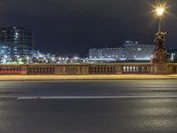 a city street next to a large bridge lit up at night by buildings and lights