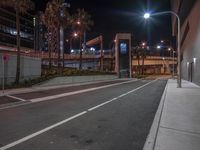 this is an empty street by a city at night time with several palm trees, buildings, and a sidewalk