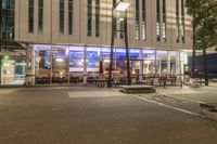 a street view at night, of a group of chairs and tables, in front of a building