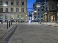 an empty paved street with multiple benches and lights in front of tall buildings in the city