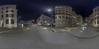 this is a 360 - lens photo of an intersection near some buildings at night with a bus going by